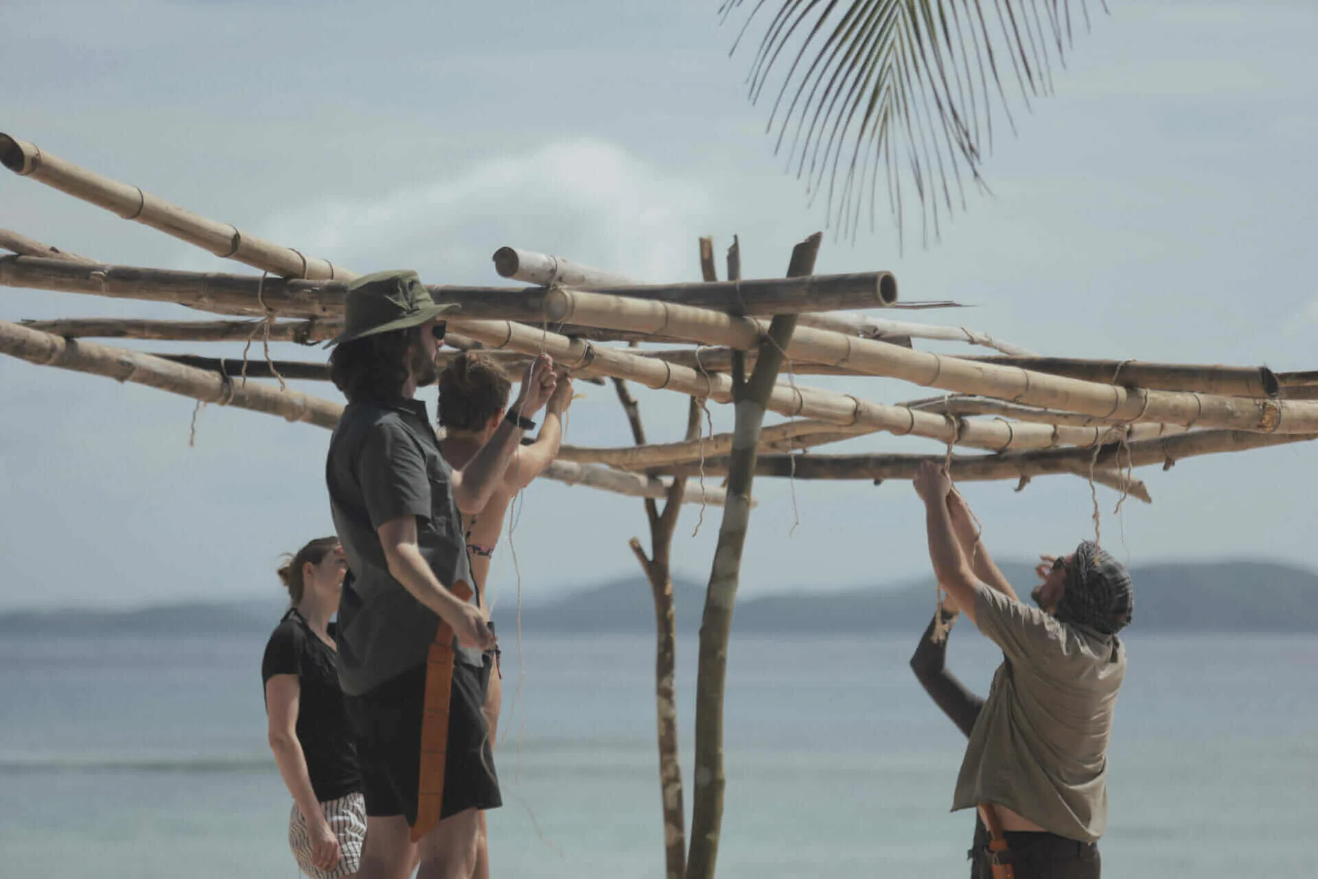 A group of people on an adventure holiday building a bamboo structure on the beach during a desert island survival.