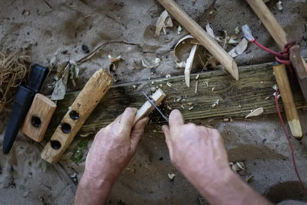 A man is working on a piece of wood in the sand.