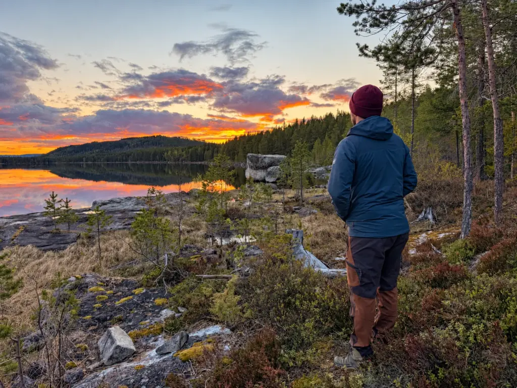 Person standing alone on a rocky shore above a lake at dusk