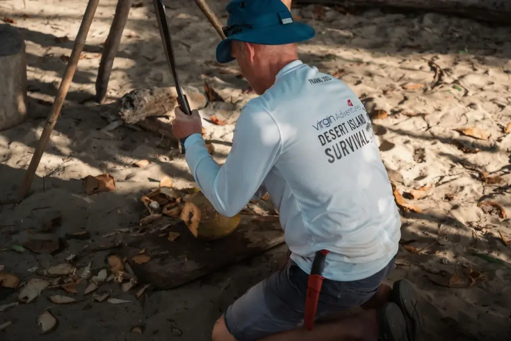 Man splitting a coconut with a machete at a beach camp