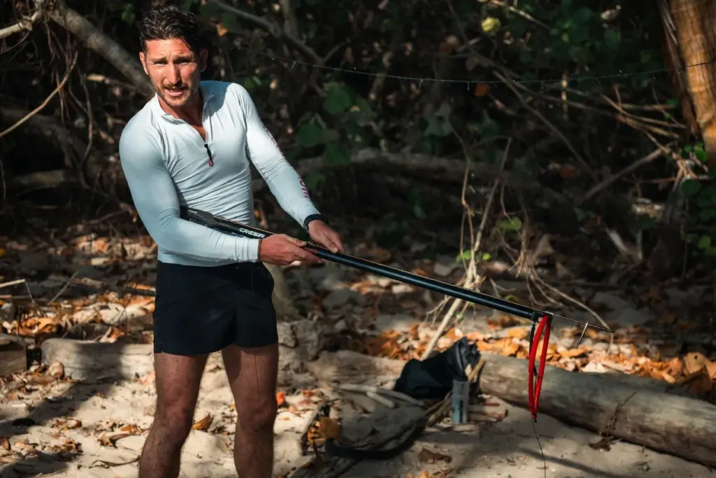 Man demonstrating a pole spear at a beach camp