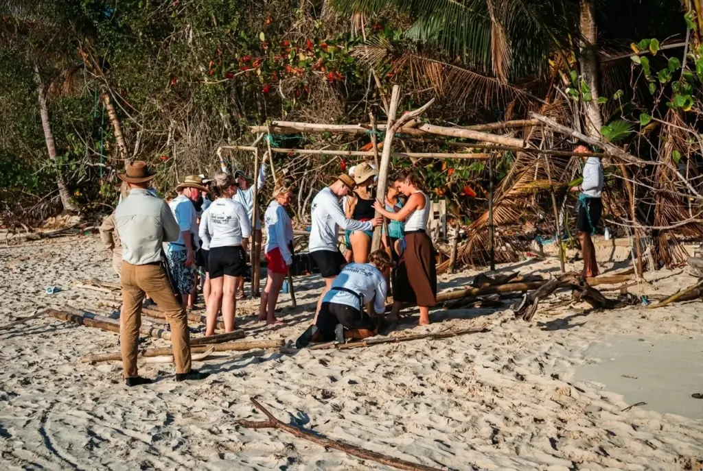 Group working together on a driftwood shelter frame on the beach
