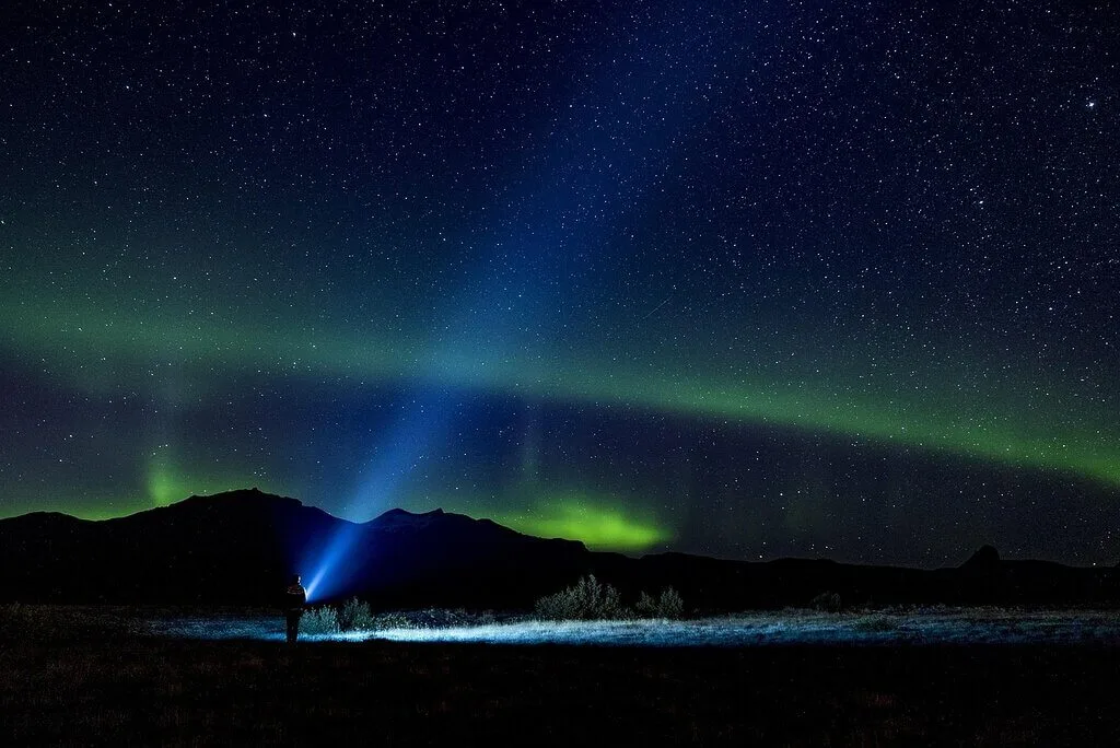 Sweden night sky with aurora borealis and a person using a flashlight