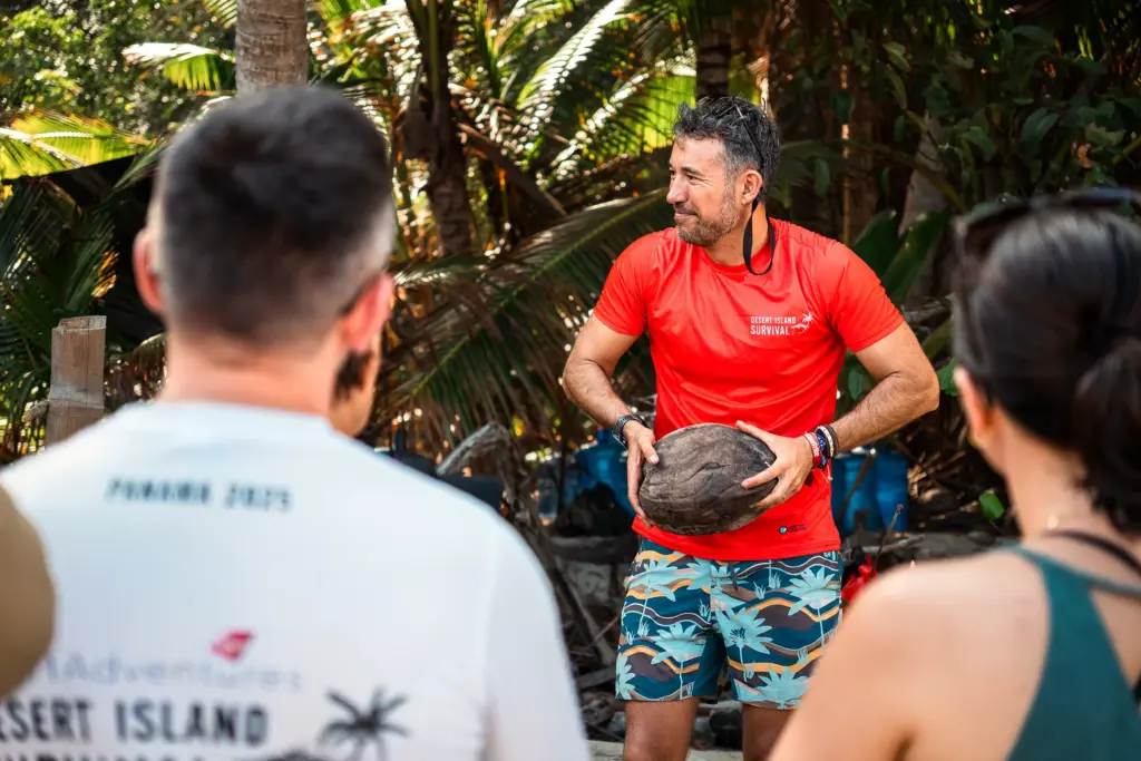 Instructor in a red shirt demonstrating a skill to a group under the palms