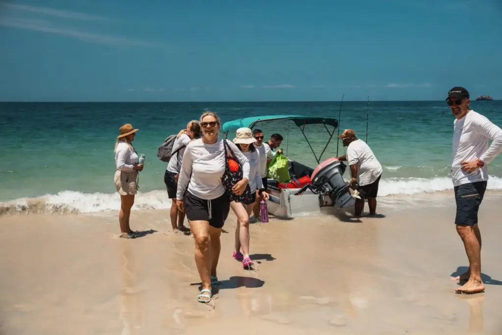 Team wading ashore from a boat onto a white sand beach