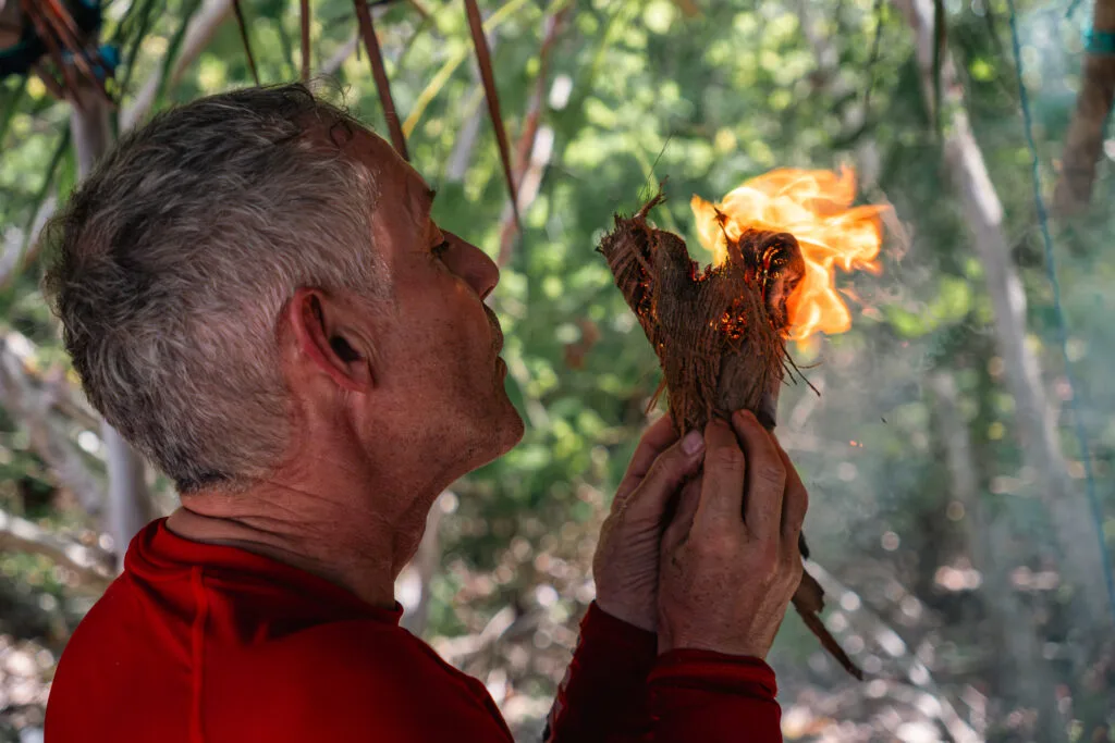 Man starting a fire with a bow drill. He's holding the burning tinder bundle.