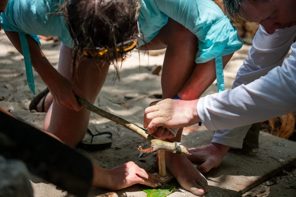 People using a bow drill to start a fire, demonstrating a survival skill.