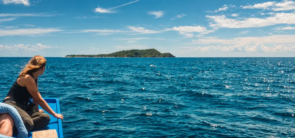 Woman on a boat looking out at a remote island across open sea