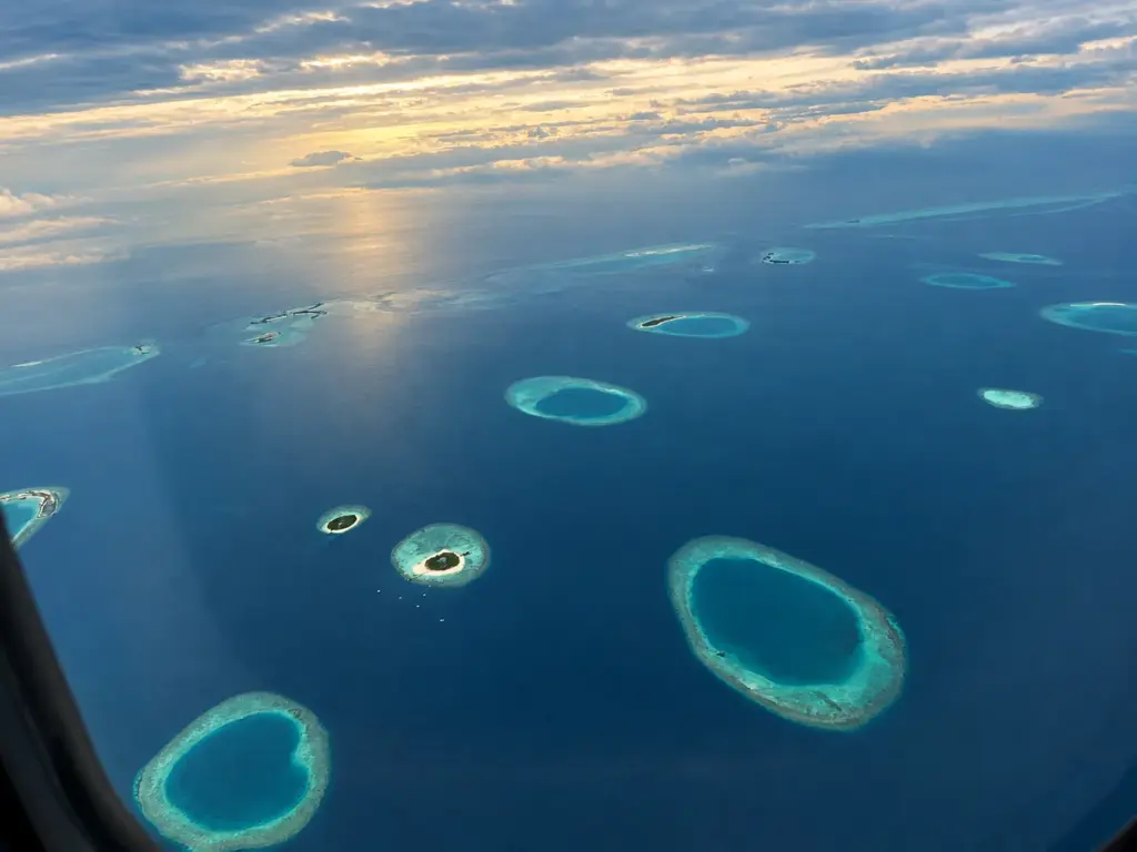 Ring-shaped coral atolls in deep blue ocean seen from a plane window over the Maldives