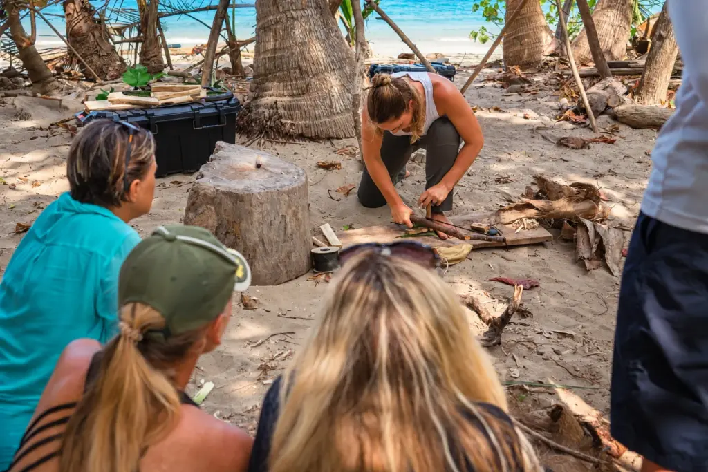 Participants watching a friction fire demonstration at a beach camp