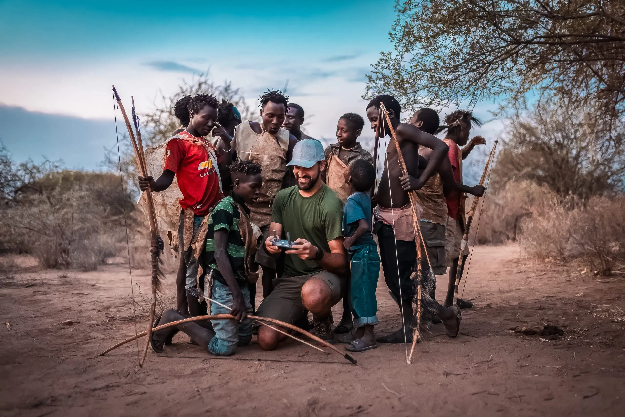 During a Hadza Tribal Bushcraft Immersion & Luxury Safari, a group stands on sandy ground outdoors—most holding.