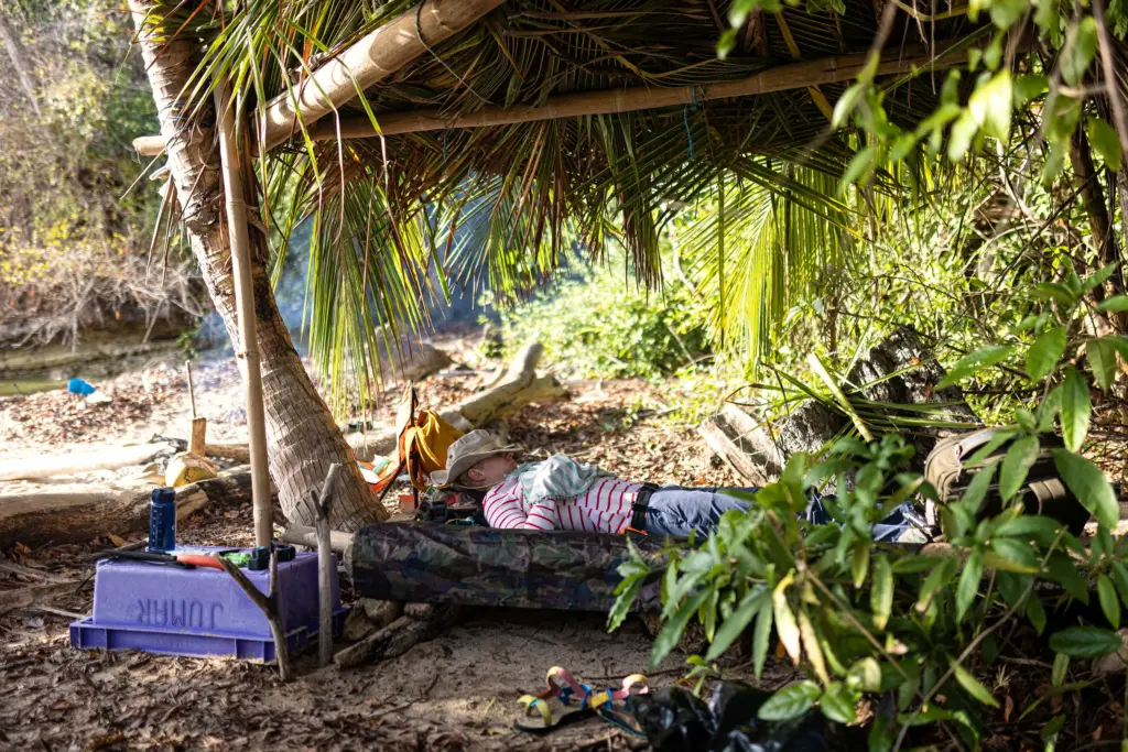 Participant resting in a hammock beneath a palm-thatch shelter at the expedition camp