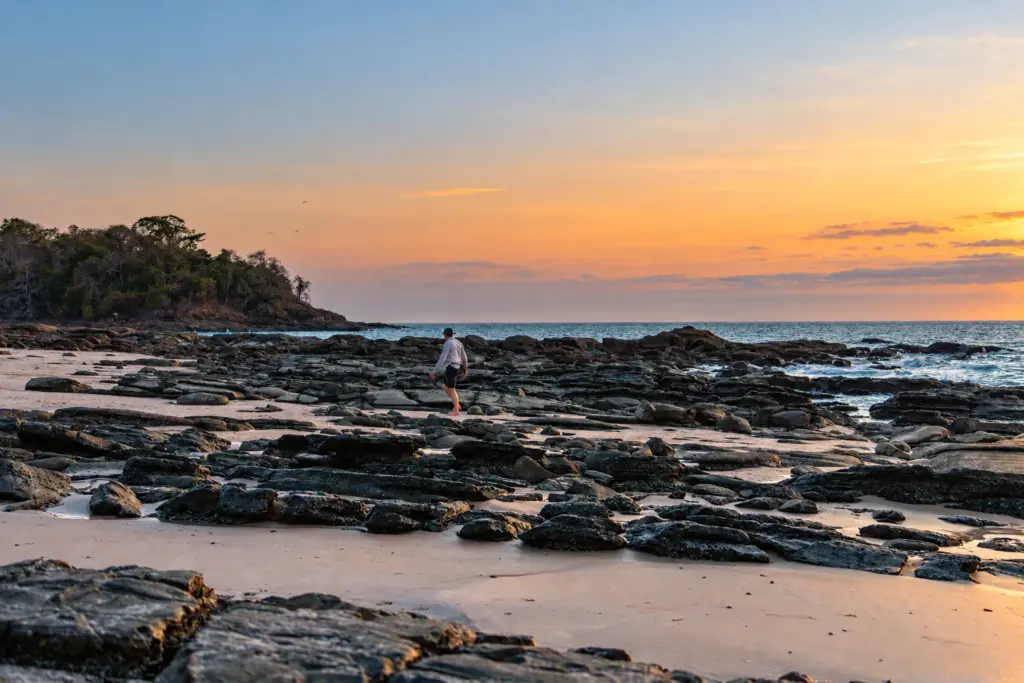 Person exploring a rocky shoreline at sunset on a desert island
