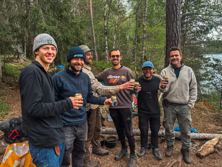 Group of friends toasting with beer cans during a Sweden survival adventure in the forest