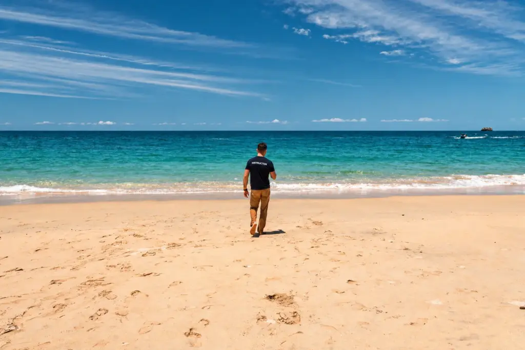 Desert Island Survival instructor walking across an empty beach towards turquoise water