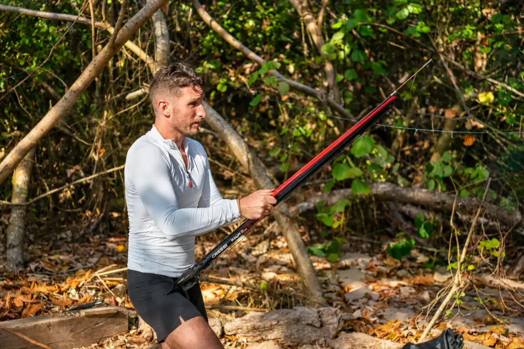 Participant holding a pole spear at the jungle edge during a spearfishing session