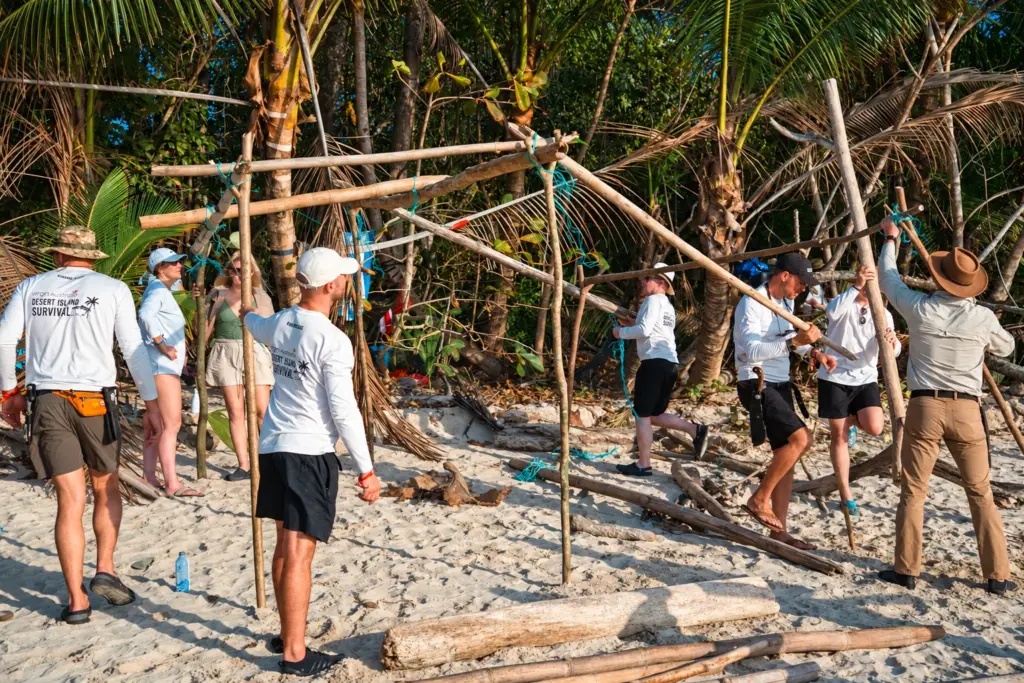 Team lifting and lashing poles to build a beach shelter together