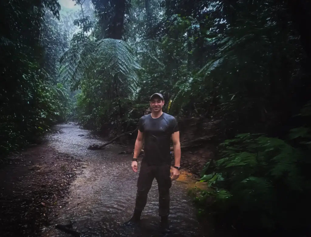 Instructor stands in a lush, rain-soaked jungle, surrounded by ferns and foliage.