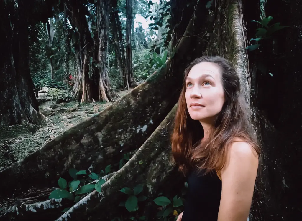 Instructor in lush jungle, looking up at trees.