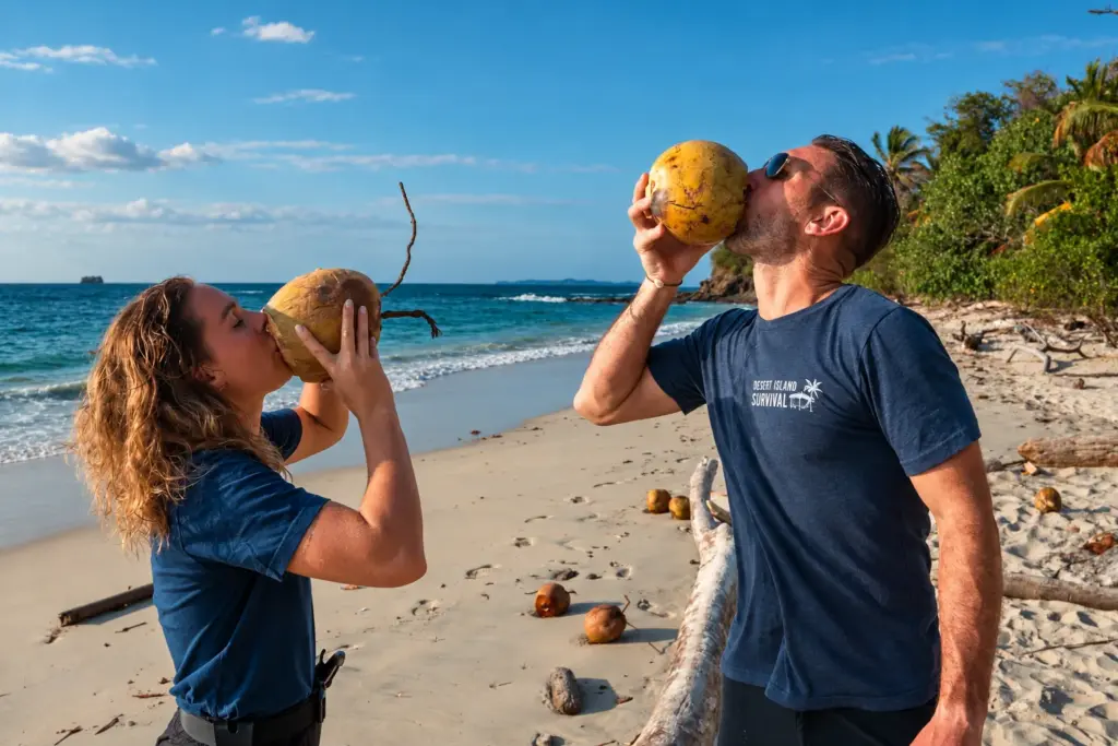 Two participants drinking fresh coconuts on a desert island beach