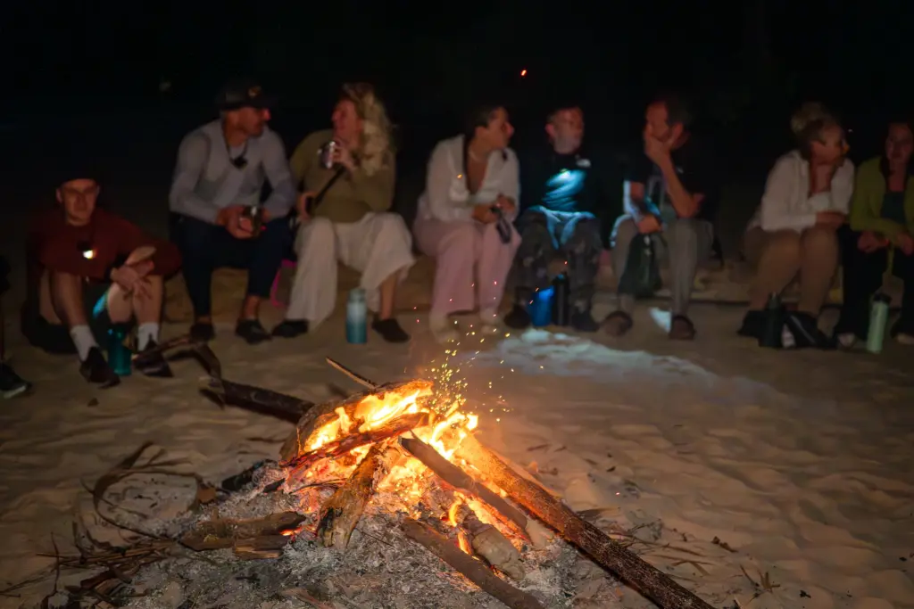 Expedition group gathered around a beach campfire at night on a desert island