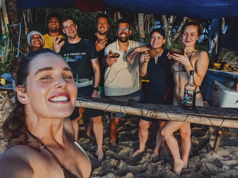 Survivors celebrating on a tropical desert island, enjoying coconuts and drinks, showcasing teamwork and survival skills.