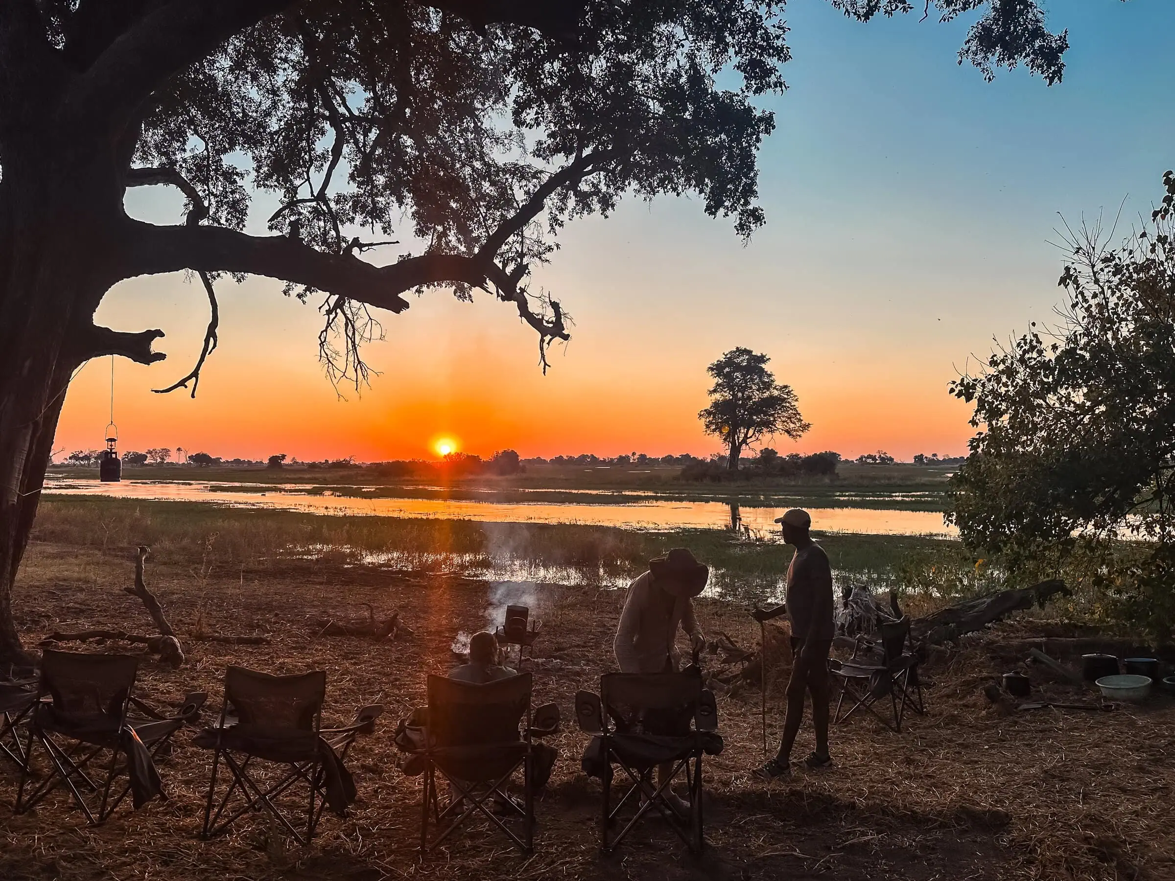 Sunset over a tranquil river on a desert island, with people camping, cooking, and enjoying nature; perfect for desert.