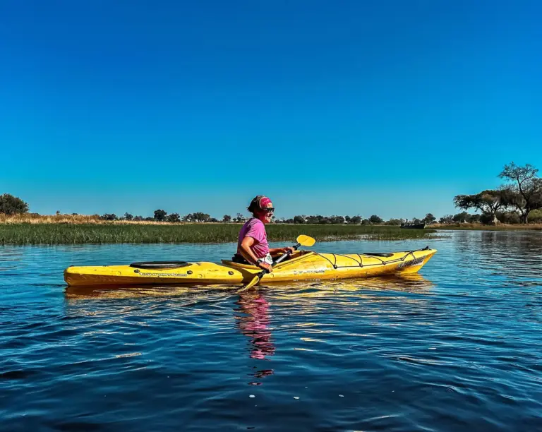 Bright yellow kayak on calm water, featuring a woman in a pink shirt and headband paddling under a clear blue sky.