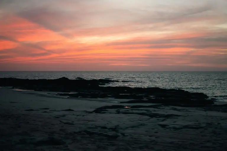 Vibrant sunset over a deserted beach with rocky shoreline, ideal for desert island survival scenarios, emphasizing ocean.