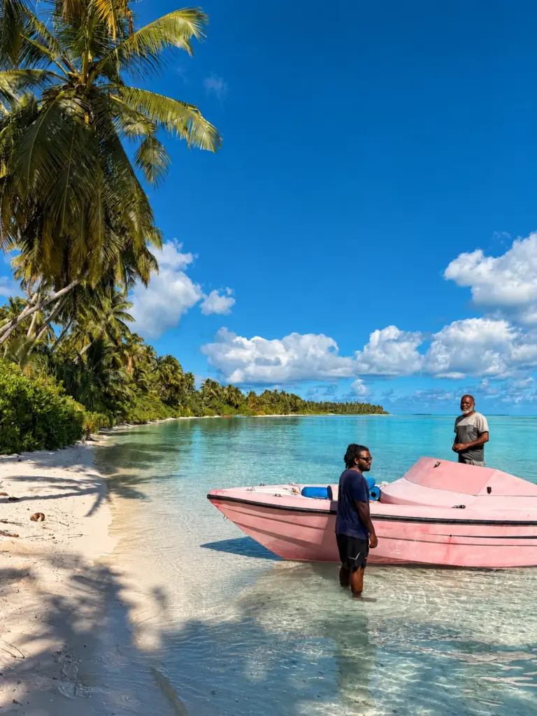 A boat pulled up on a palm-fringed beach in a turquoise lagoon
