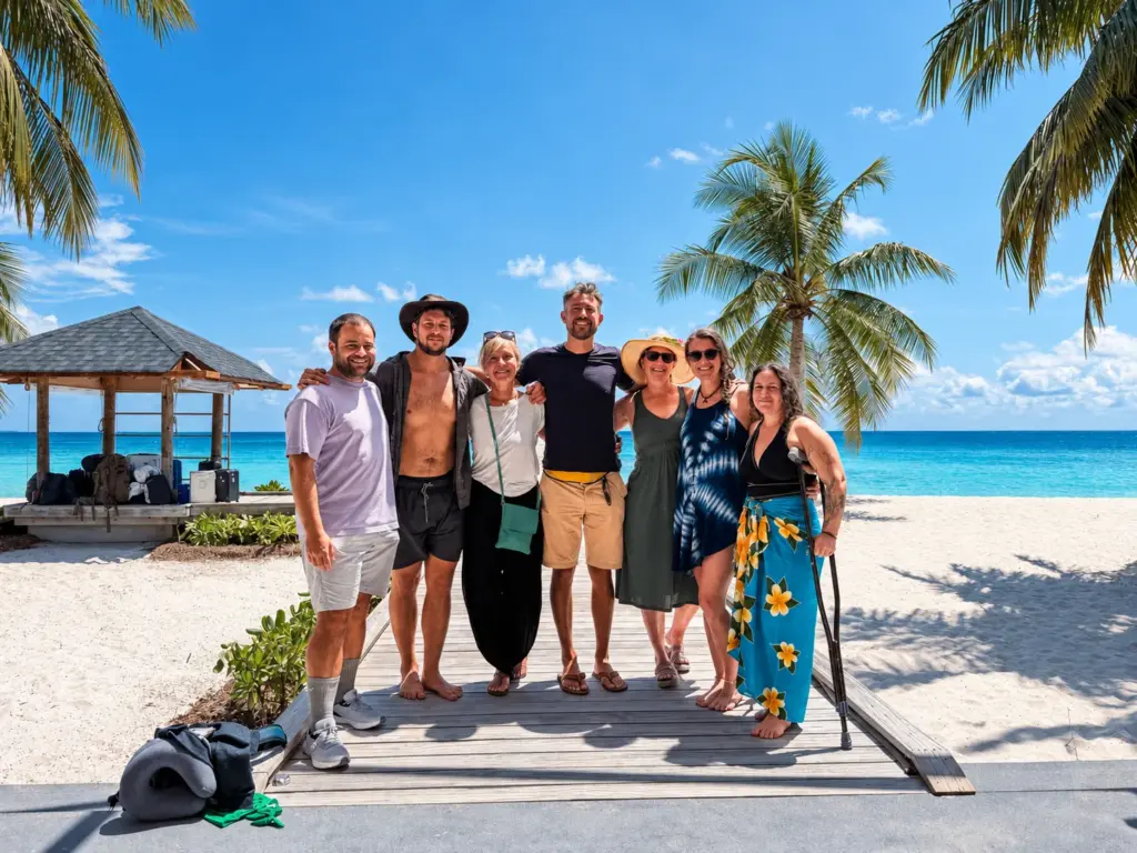 The group together on the beach in front of palm trees and a lagoon