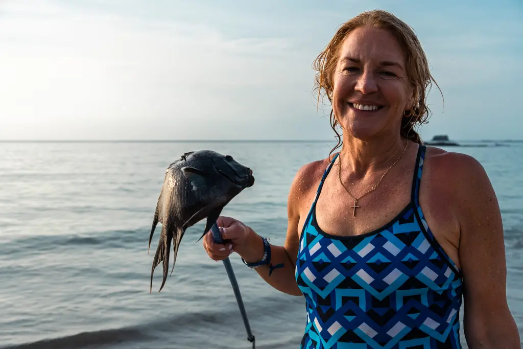 Woman in Panama holding a fish on a spear, smiling after survival fishing.