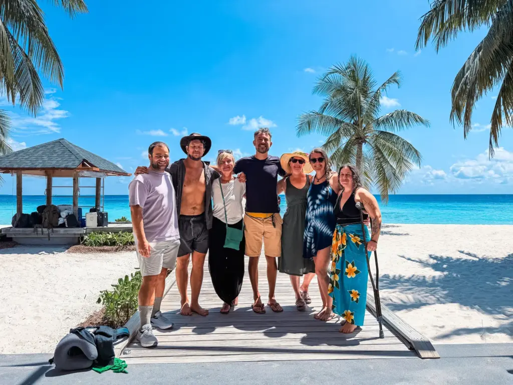 Group of people on a sandy beach, possibly after a cleanup, cloudy sky.