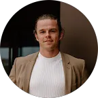 Man with blonde hair pulled back, wearing a tan blazer over a white shirt.