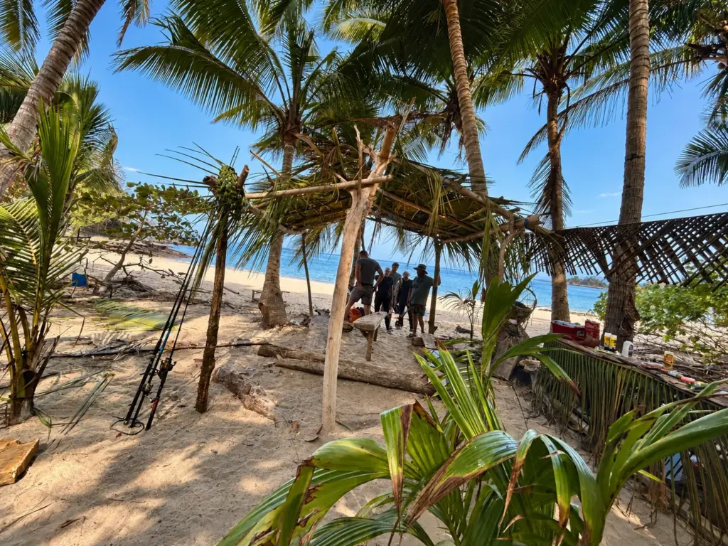 A finished palm-leaf shelter on the beach beneath coconut palms