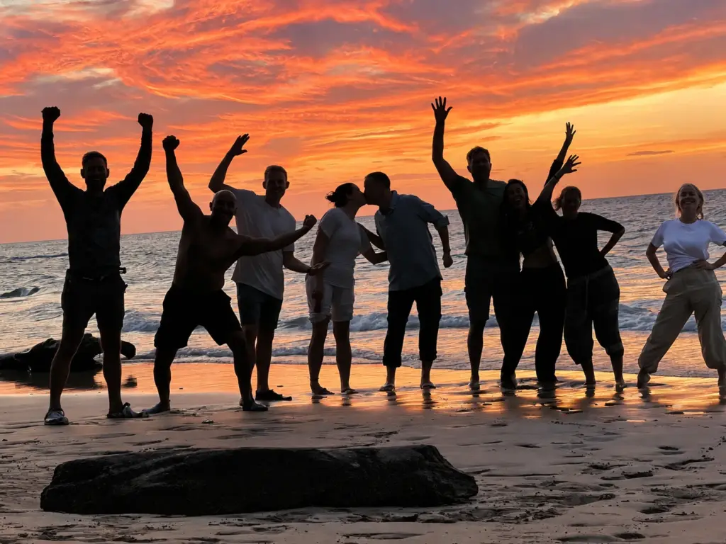 A group of friends are celebrating the sunset on the beach.  Silhouetted against the vibrant orange and pink sky, they are posing and enjoying the beautiful moment together.  The image captures a sense of joy and camaraderie as they share this special time.