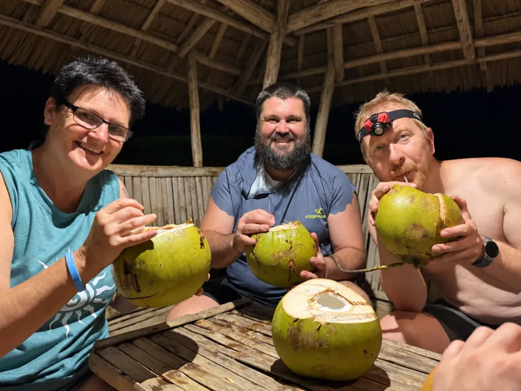 Three participants enjoy fresh coconuts in a bamboo hut