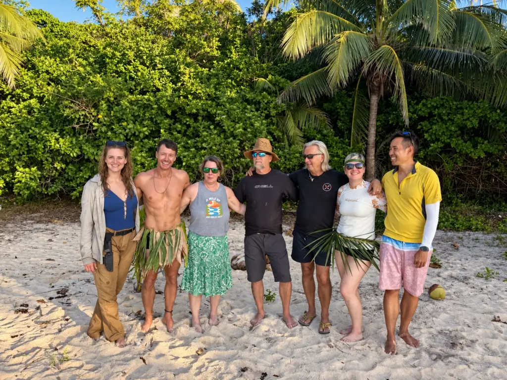The group in handmade grass skirts on a white sand beach