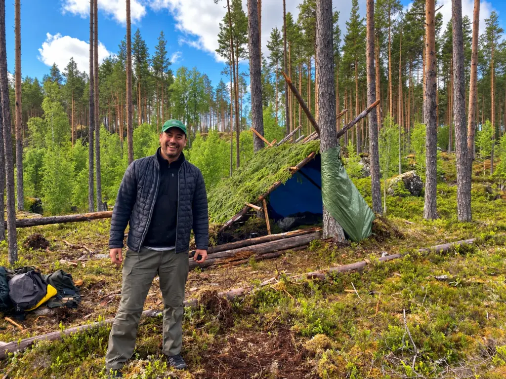 A participant stands in front of his hand-built forest shelter