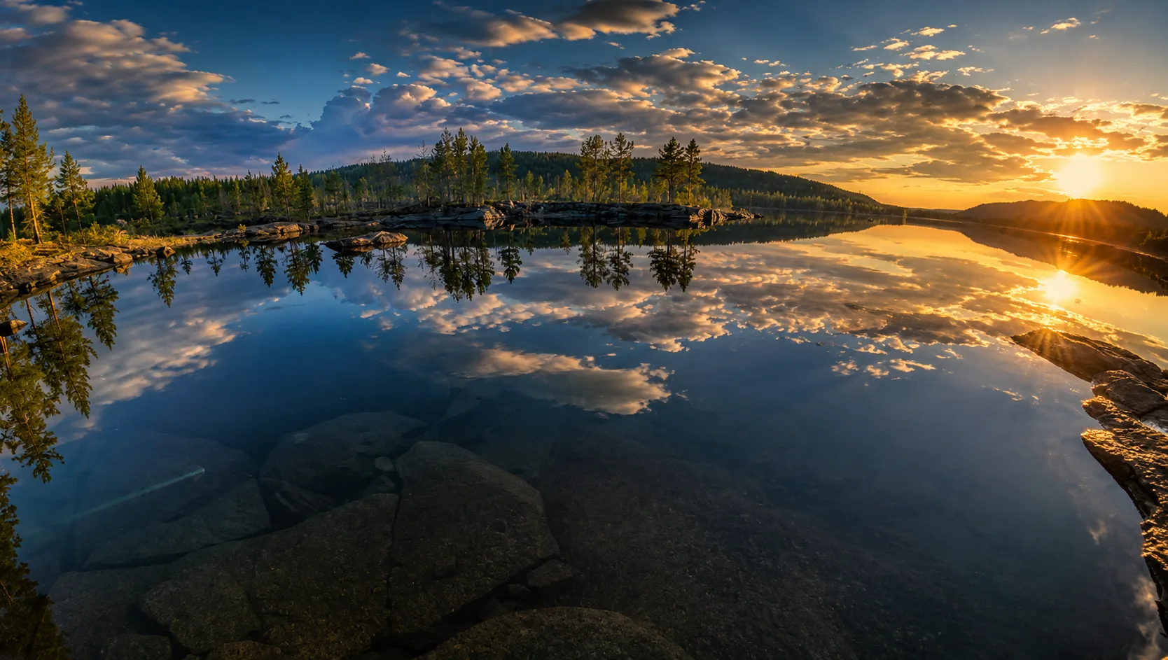 Sunset over a calm lake reflecting trees and clouds in Sweden