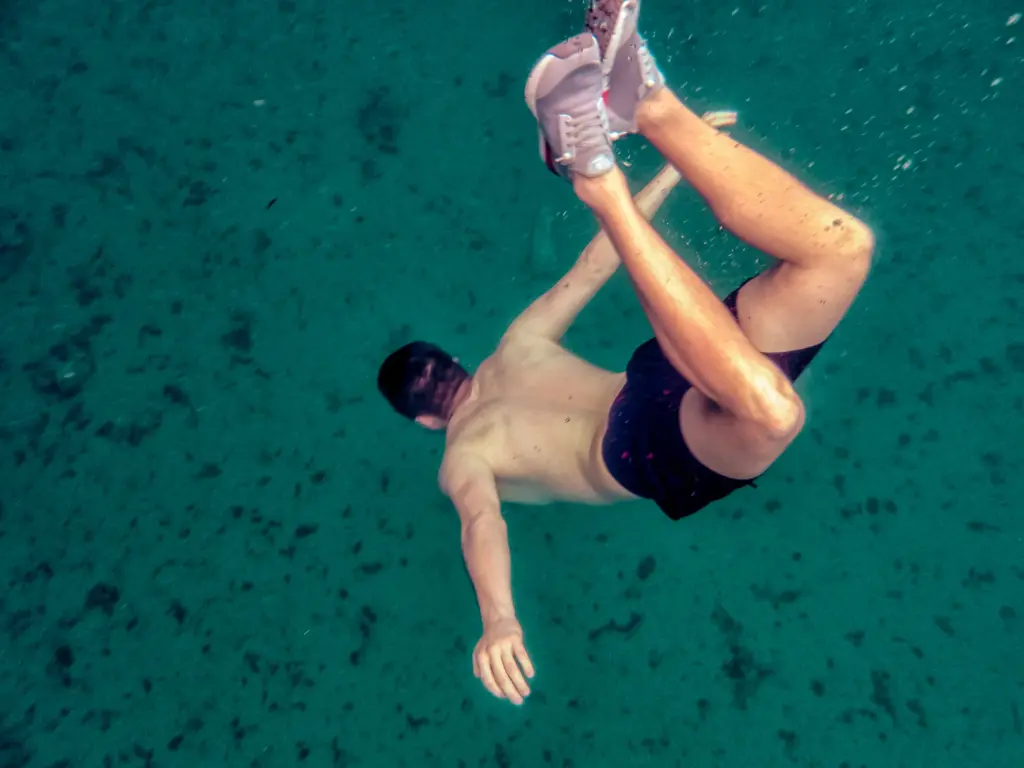 Man diving underwater with shoes on, survival expedition concept.
