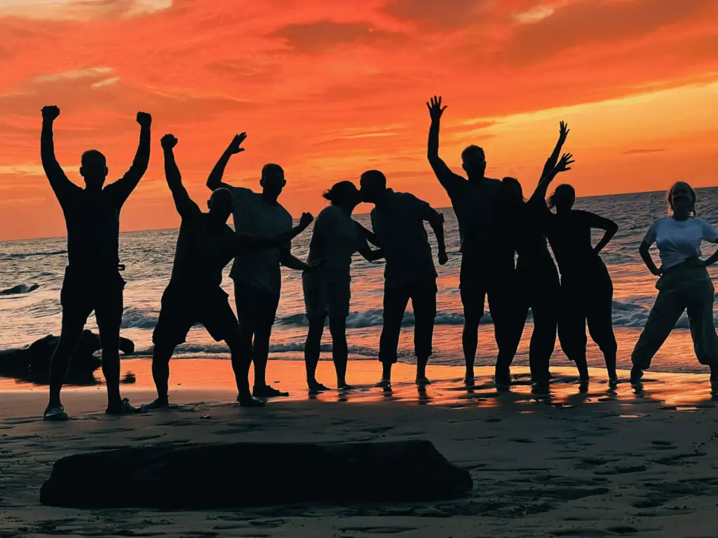 Group of people silhouetted against a vibrant sunset on a beach. Celebration scene.