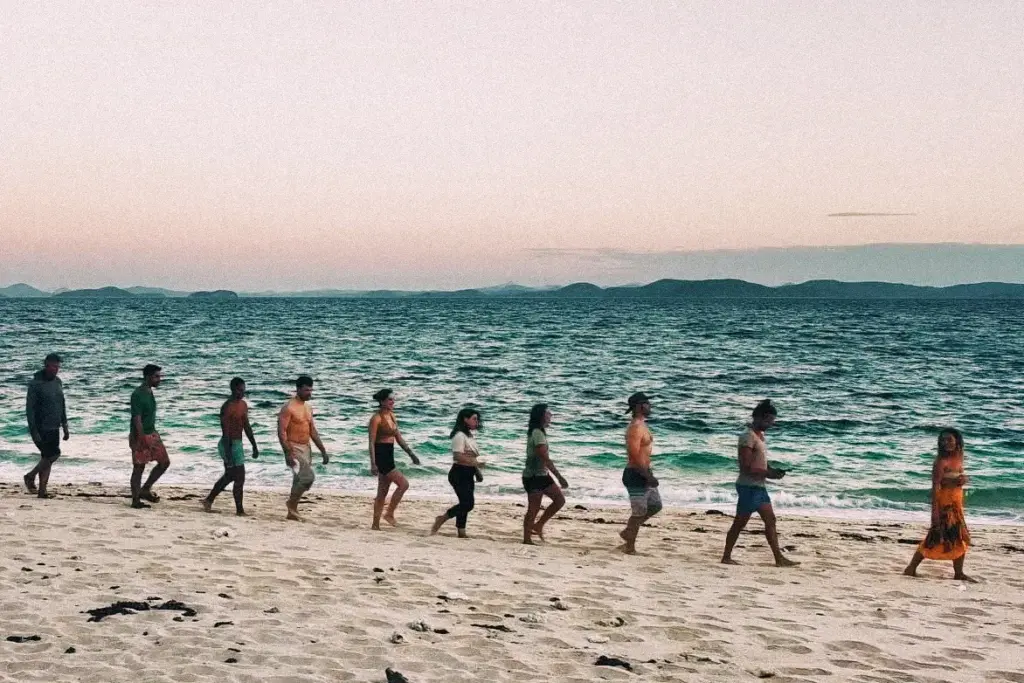 Group of people walking on a sandy beach next to ocean water.