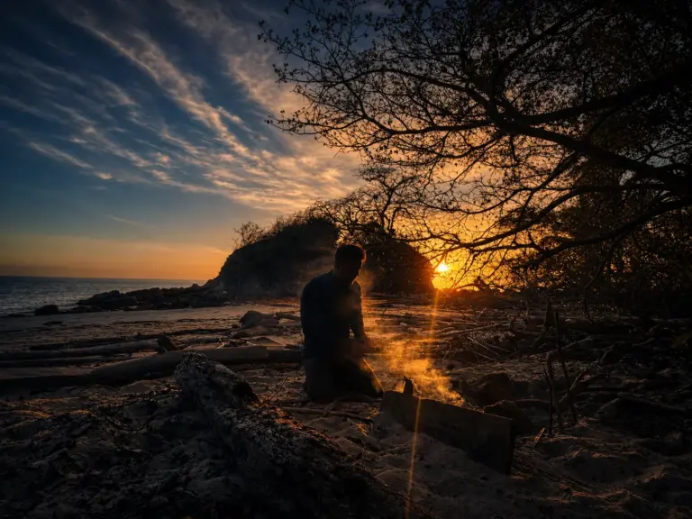Tom by campfire on beach at sunset, reflecting on micro-retirement