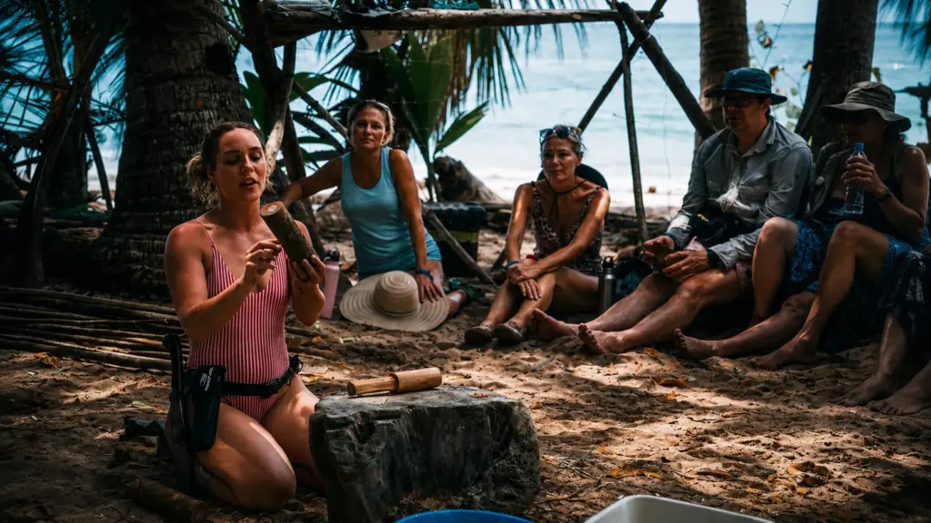 Smiling woman in black swimsuit on a tropical beach with raw fish