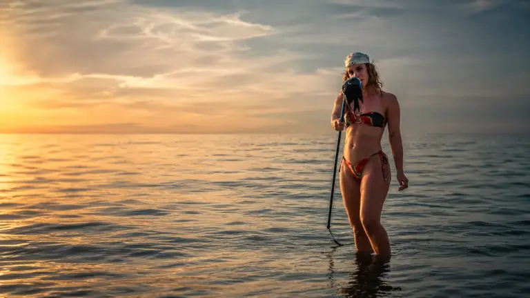 Woman in bikini sings into microphone in the ocean at sunset