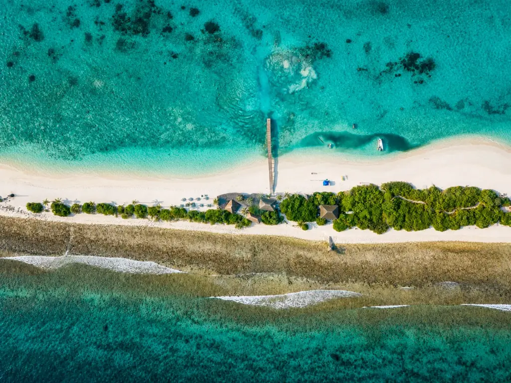 Aerial view of a narrow Maldivian island with a pier, turquoise water, and white sand beaches.