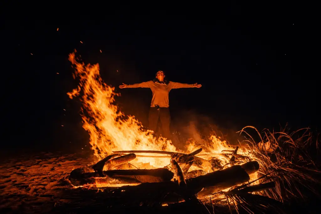 Person with arms outstretched in front of a large bonfire at night