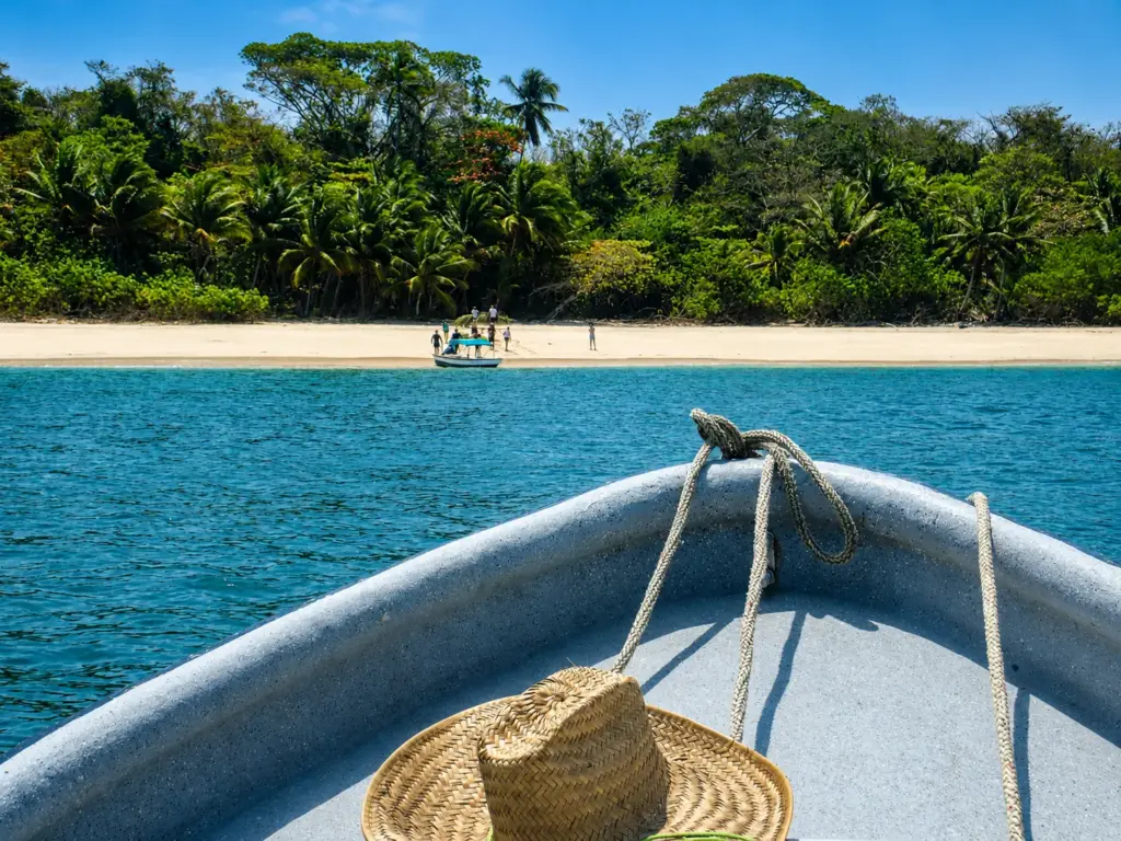 Boat approaching a tropical beach with palm trees and people on shore.