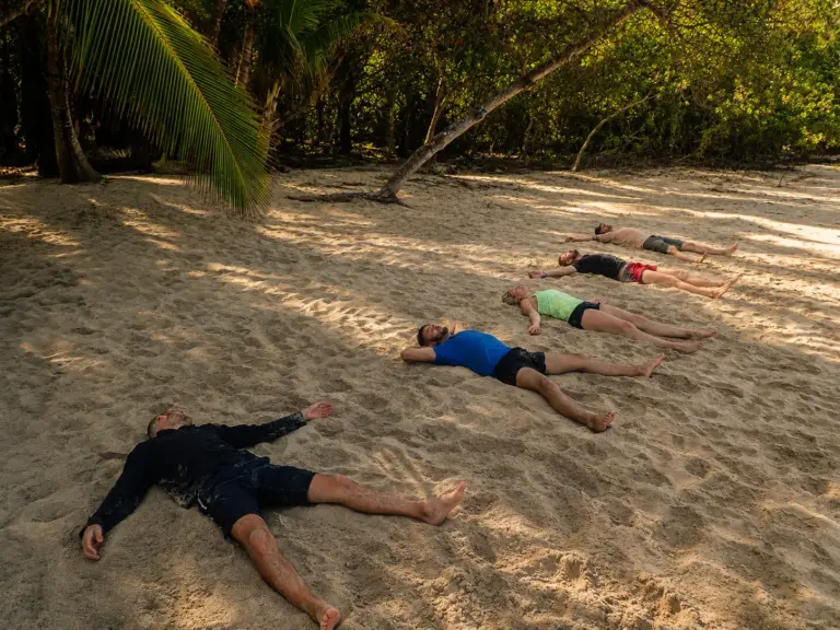 People lying on a sandy beach in a yoga pose.
